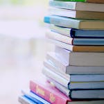 A tall stack of colorful hardcover books on a table indoors, perfect for library-themed concepts.