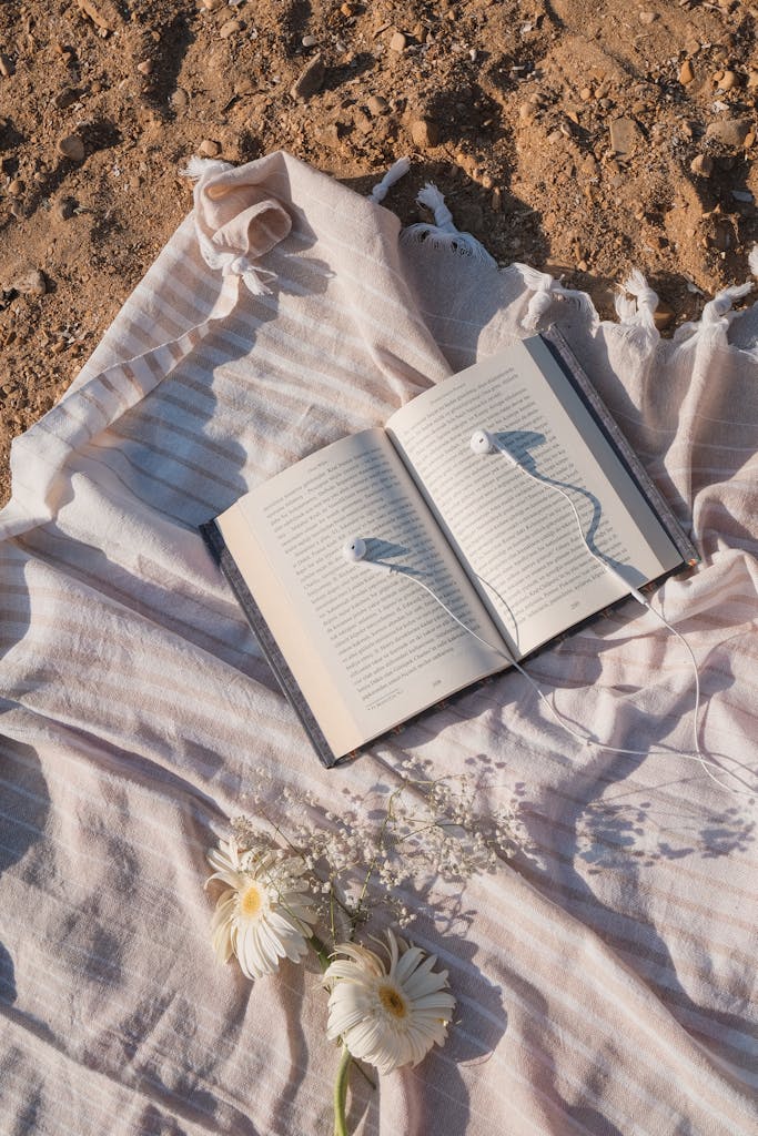 Book, Headphones and Flowers on Blanket on Beach